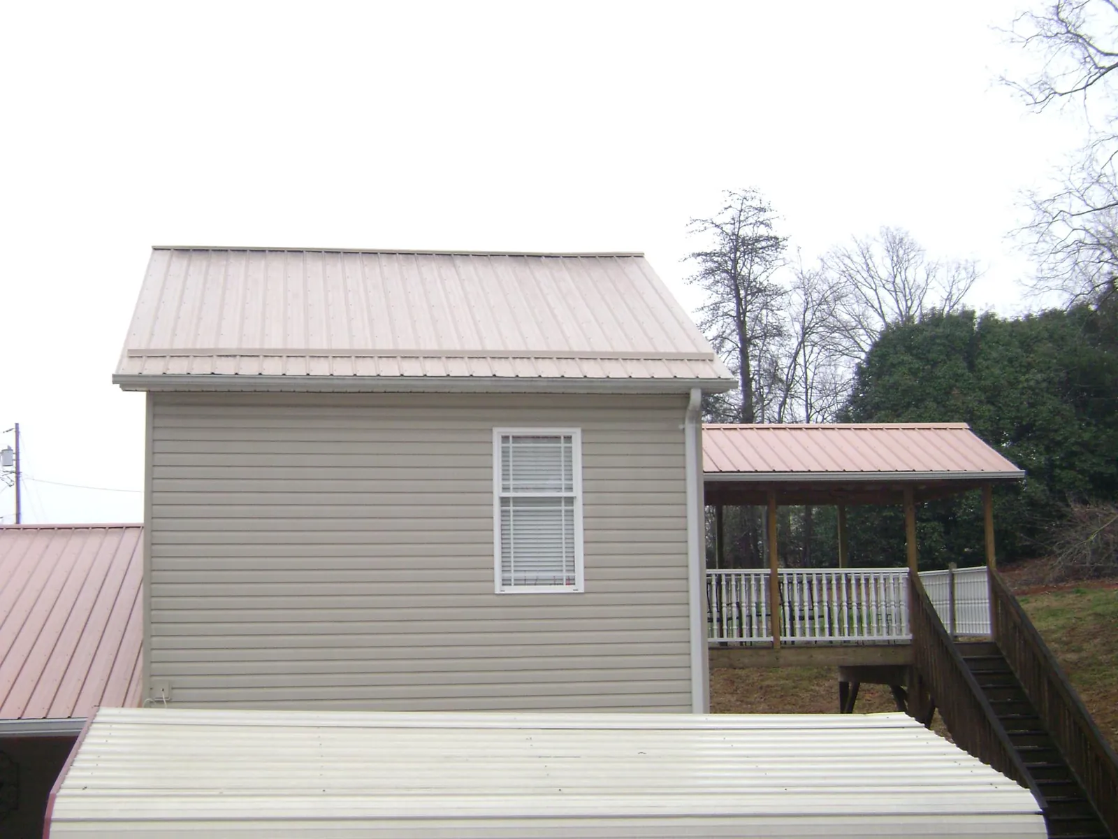 Tan metal roofs on a two story addition and attached porch, from a Roof Replacement job in Jasper